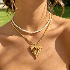 Close-up detail of layered gold snake chain necklace with textured heart pendant and pearl choker.