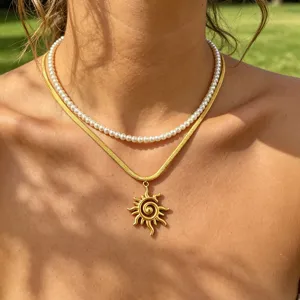 Close-up detail of double layer pearl and gold snake chain necklace with sun pendant.