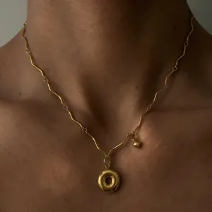 Nahaufnahme Detailaufnahme einer vergoldeten Wellenkettenkette mit einem Donut-Anhänger.
