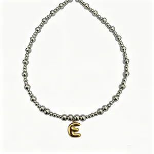 Detailed shot of trendy stainless steel beaded necklace with gold bubble letter E pendant.