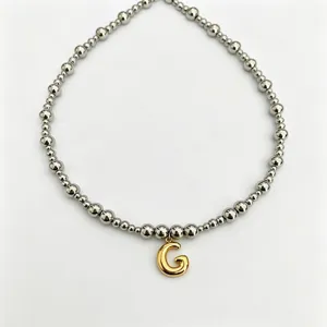 Detailed close-up of stainless steel beaded necklace featuring a stylish gold letter G pendant.
