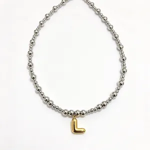Close-up detail of silver stainless steel beaded necklace with gold bubble letter L pendant.