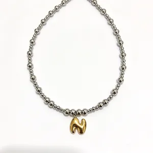 Stainless steel beaded necklace detail featuring a trendy gold bubble letter pendant stylish.
