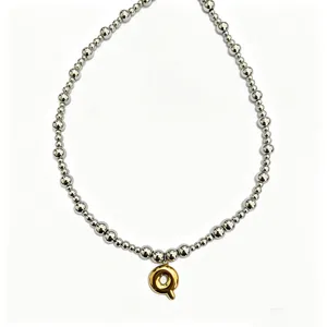 Close-up detail shot of the silver bead necklace featuring a glossy gold bubble letter pendant.