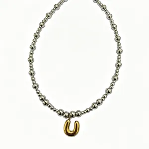 Close-up detail of silver bead chain necklace featuring a bold gold bubble letter U pendant.