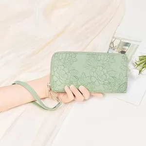 Close-up view of the embossed floral mint green long zip wallet with a matching wrist strap.