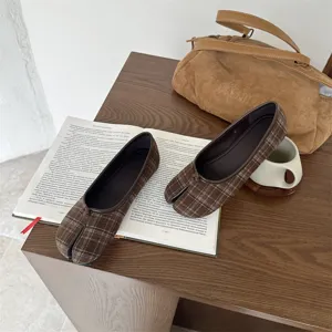 Primo piano dettagliato di scarpe basse tabi divise a quadri marroni su tavolo in legno.