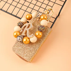Estuche de llaves de cuero brillante con correa de cuentas y colgante de strass.