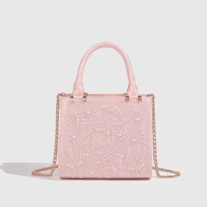 Detalle de bolso de mano de saten rosa con bordado de perlas, cadena elegante y asa.