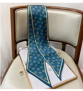 Dettaglio di foulard in seta sottile blu scuro con bordo dorato e stampa monogramma.