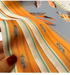 Primo piano di un foulard in seta a righe arancioni da donna con stampa di piume morbide.