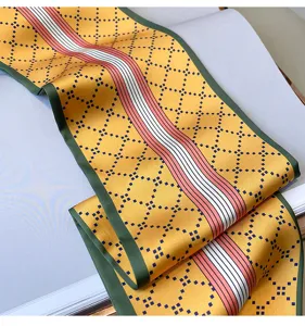 Primo piano dettagliato di una sciarpa in seta gialla stretta con bordo verde e motivo geometrico.