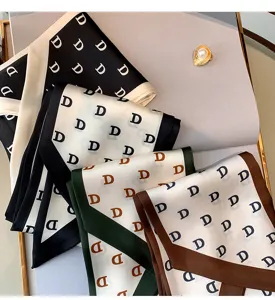 Detail view of the elegant narrow silk scarf featuring repeating letter print for stylish wear.