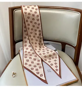 Dettaglio di un elegante foulard twilly beige con monogramma e bordo marrone su sedia.