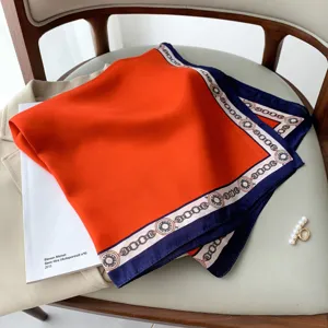 Primo piano del foulard di seta arancione con una raffinata bordatura a catena blu scuro.