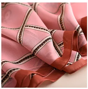 Primo piano di foulard in seta sintetica rosa con motivo a catena e bordo marrone.