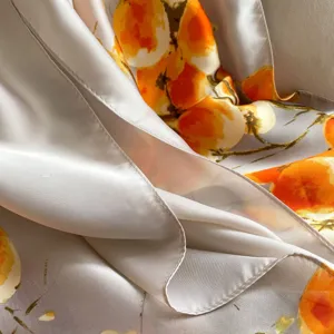 Primo piano dettaglio tessuto foulard in seta con stampa floreale arancione e orlo.