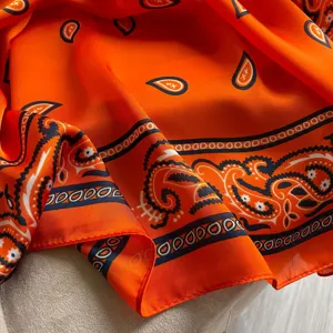 Orange paisley print scarf detail, lightweight summer beach shawl fabric texture close-up.