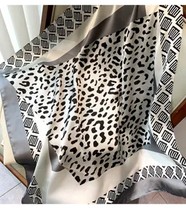 Primo piano di un foulard elegante con stampa leopardata e bordi geometrici, tessuto morbido.