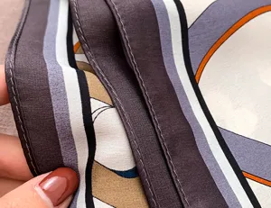 Close-up detail shot of the elegant silk scarf, highlighting exquisite rolled hems and fine fabric texture.