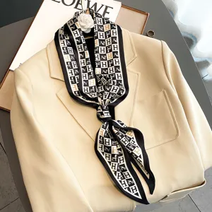 Detailed view of a stylish black, white and gold silk-feel scarf draped on a chic beige blazer.