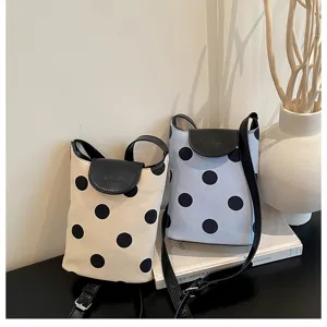 Polka dot linen splice bucket bag detail showcasing black leather flap and adjustable strap.