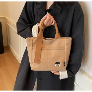 Detailed view of the khaki canvas tote bag featuring front pocket and cute cartoon patch.