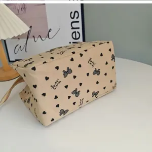 Detail view of a stylish beige canvas handbag featuring a cute black bow and heart print.