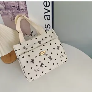 Detail view of a stylish canvas handbag featuring cute black heart and bow prints, twin handles.