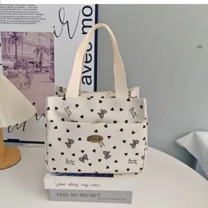 Canvas tote bag detail showing heart and bow print, front pocket and sturdy fabric handles.