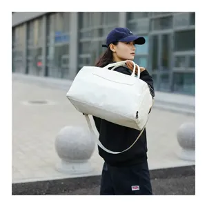 Detail view of a large capacity white travel duffle bag carried outdoors by a model.