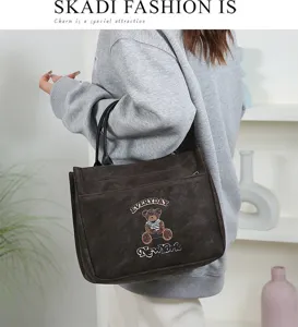 Vue détaillée d'un grand sac cabas en PU marron foncé avec joli patch ours et bandoulière.