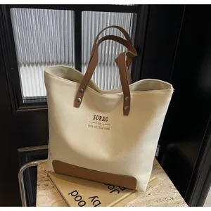 Minimalist canvas tote bag with brown leather handles for women commuting and casual daily use.