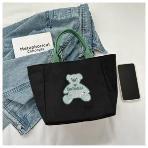 Black canvas tote bag with green handles and stylish bear graphic design detail shot.