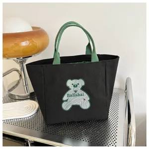 Black canvas tote bag with green handles and cute bear patch design for daily casual use.