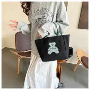 Black canvas tote bag with green handles and cute bear graphic, stylish casual shoulder bag.