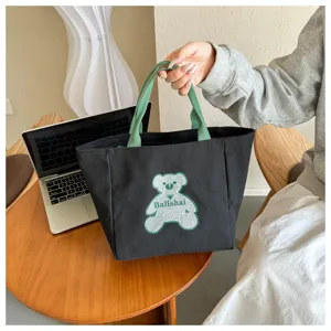 Detail shot of black canvas tote bag featuring green handles and cute line art bear graphic.