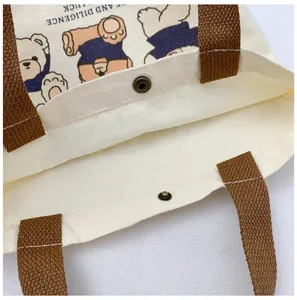 Canvas tote bag detail, featuring durable brown handles, metal snap button closure and cute bear print.