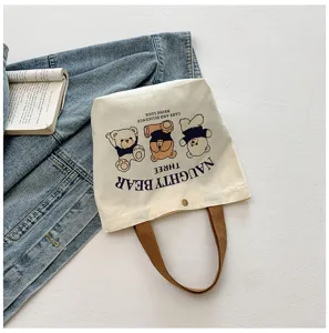 Close-up detail of cute cartoon bear canvas tote bag with brown handles on textured surface.