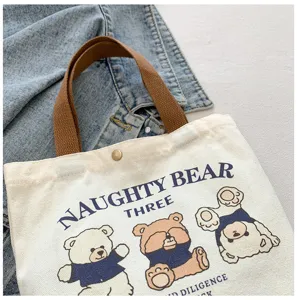 Canvas tote bag detail view, casual shoulder handbag with cute cartoon bear print and handles.