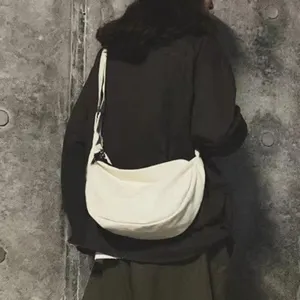 Detail view of white canvas crossbody messenger bag worn by person in industrial setting.