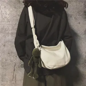 Minimalist white canvas crossbody bag with cute green frog pendant, casual shoulder sling bag.