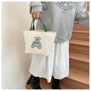 Detailed shot of the cute canvas tote bag featuring a bear print, held by a model on stairs.