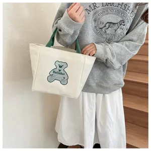Casual white canvas tote bag featuring green handles and cute bear print for daily use.