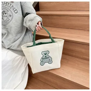 Canvas tote bag detail showing green handles, cute bear graphic print, and textured fabric.