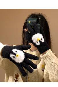 Close-up detail of cute penguin plush knitted gloves worn on hand, soft winter warm accessory.