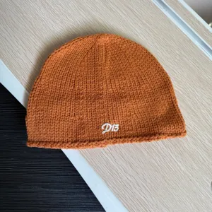Nahaufnahme einer stylischen orangefarbenen Strickmütze mit weißer Stickerei für den Winter.
