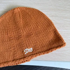 Detailansicht einer braunen Strickmütze mit besticktem Buchstaben D15 für kalte Wintertage.