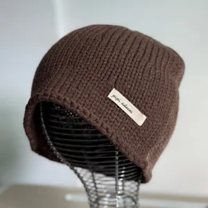 Detailansicht der braunen Strickmütze, die feine Textur und das Stoffetikett betonen.