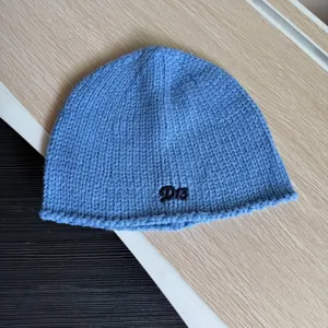 Nahaufnahme einer blauen Strickmütze mit gesticktem Buchstaben, kuscheliges Winteraccessoire.